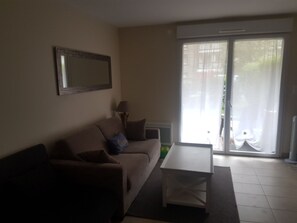 Ein Wohnzimmer mit einer Couch, einem Couchtisch, einer Lampe und einer Schiebetür zu einem Außenbereich.
