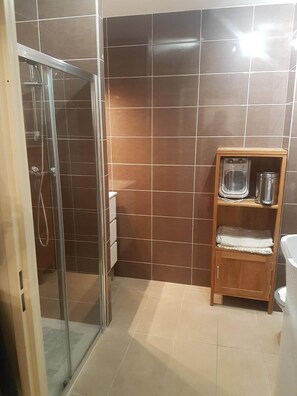 Ein Badezimmer mit einer gläsernen Duschkabine, einem Holzregal mit Heizung und einem weißen Waschbecken.