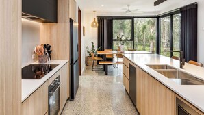 A modern kitchen with a central island, wooden cabinetry, and a dining area with a view of the outdoors.