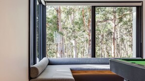 A pool table in a room with a large window overlooking a forest.
