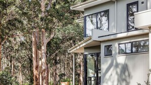 A modern two-story house with large windows and a balcony, surrounded by tall eucalyptus trees.