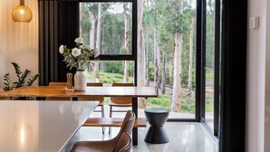 A modern dining area with a large window, a wooden table, and a vase of flowers.