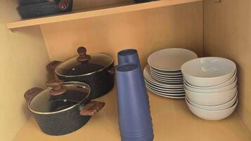 A kitchen with wooden shelves, black cookware, a blue water bottle, and stacked white plates.