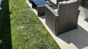 Eine Terrasse mit Korbmöbeln und einem Glastisch, umgeben von einem weißen Zaun und einem gepflegten Rasen.