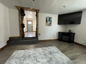 Una sala de estar con una puerta grande de madera, un televisor de pantalla plana en la pared y una alfombra mullida en el suelo.