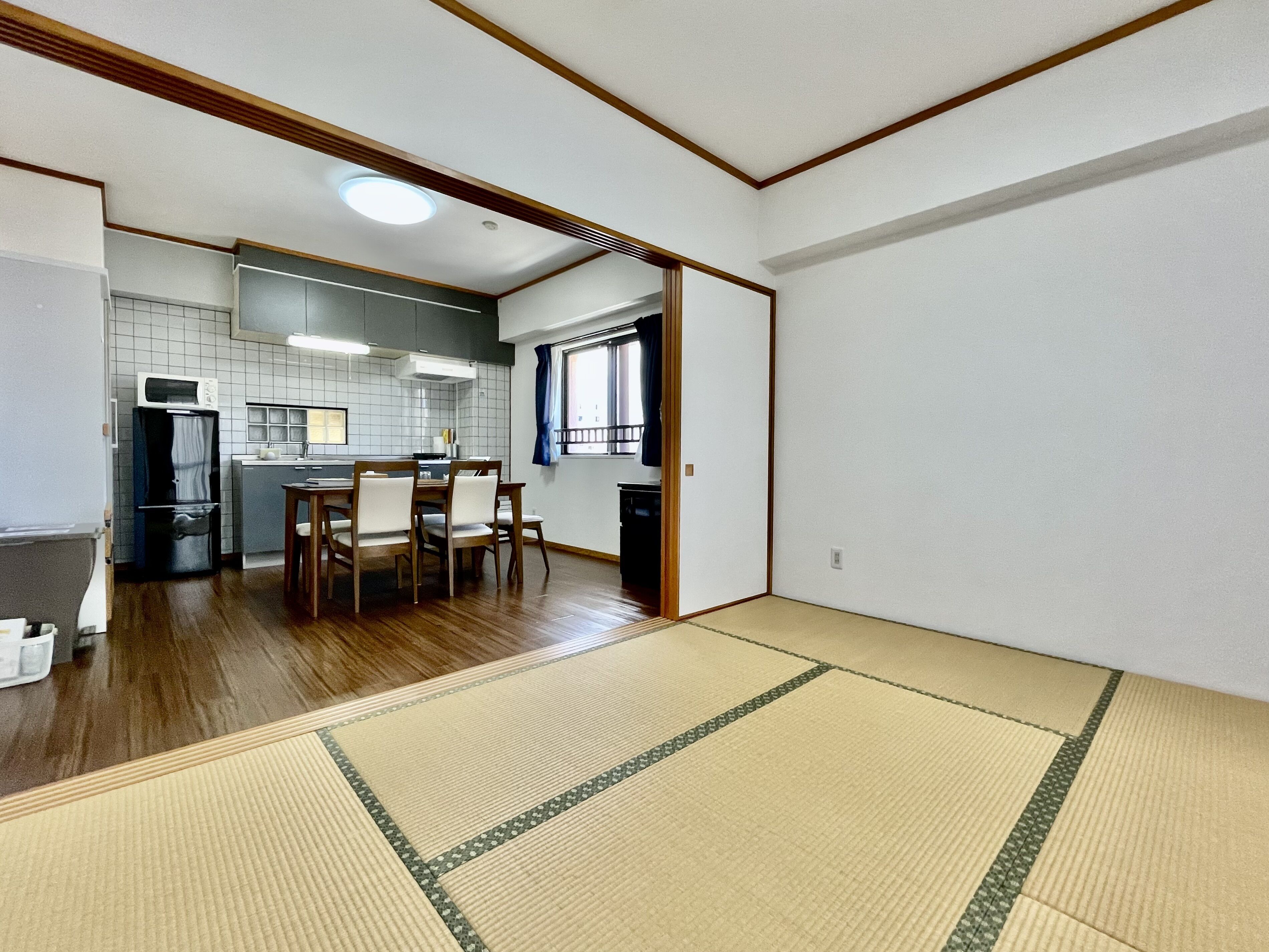 A traditional Japanese-style room with tatami flooring, a kitchen area with a refrigerator, microwave, and sink, and a dining table with chairs.