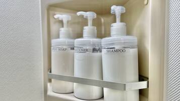 A bathroom shelf with three bottles labeled body soap, conditioner, and shampoo.
