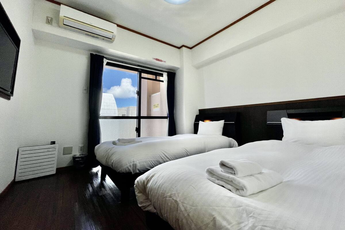 Ein Hotelzimmer mit zwei Betten, einem Fenster mit Aussicht, einer Klimaanlage und einer Deckenleuchte.