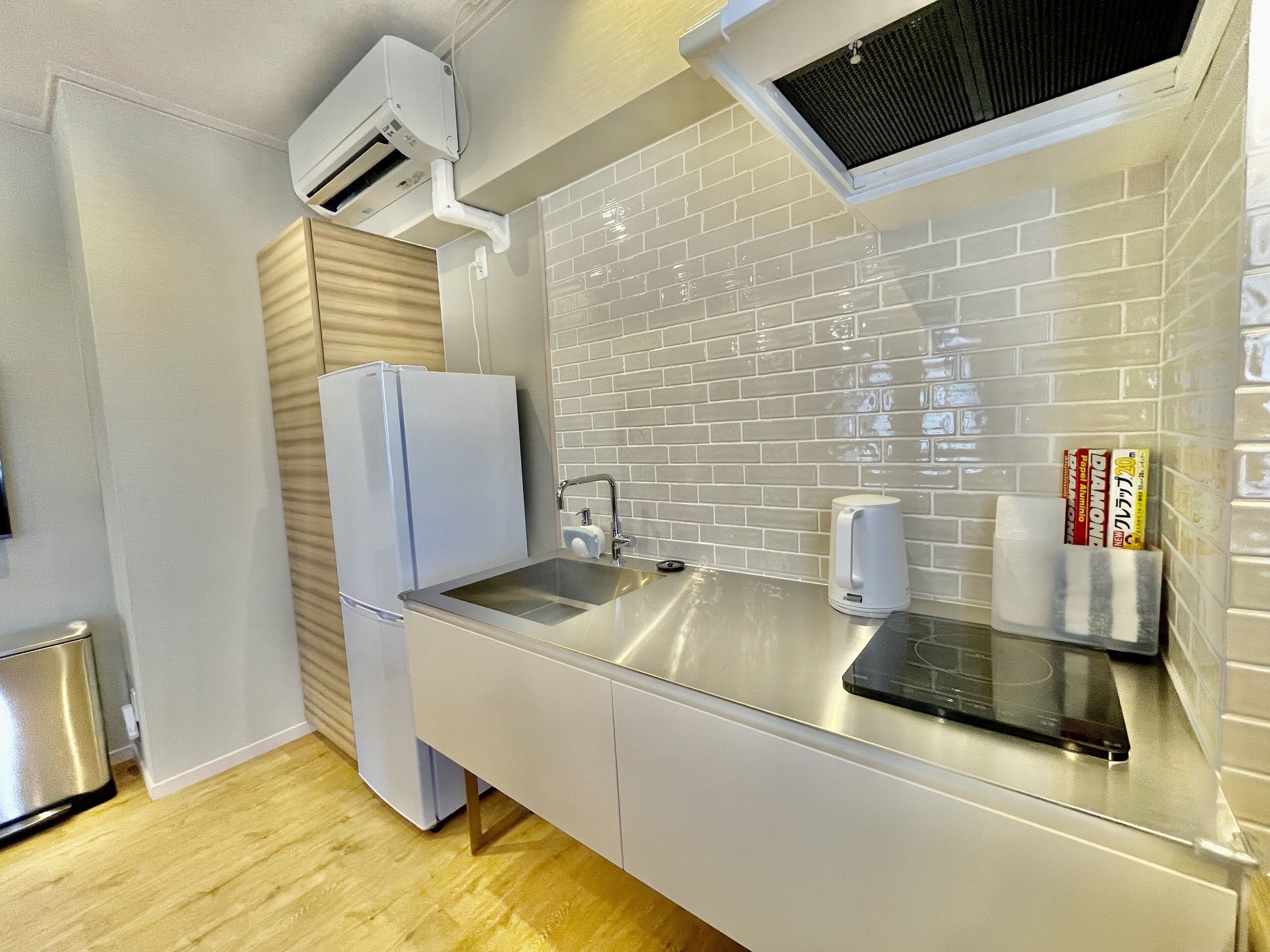 A modern kitchen with a stainless steel countertop, a built-in oven, a refrigerator, and a window with a black screen.
