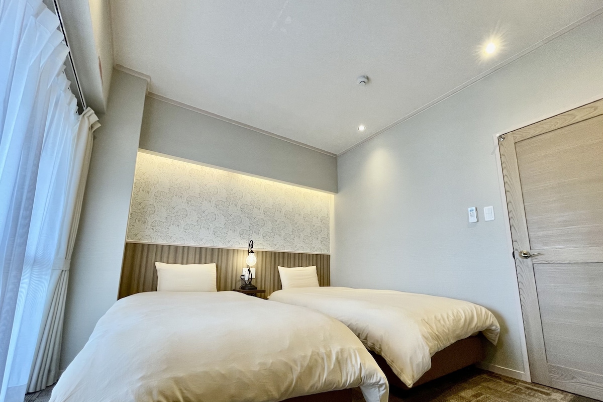 A hotel room with two beds, a nightstand with a lamp, a large mirror, and a door with a lock.