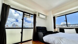Quarto de hotel com uma cama, uma cadeira e uma janela grande com vista para a cidade.