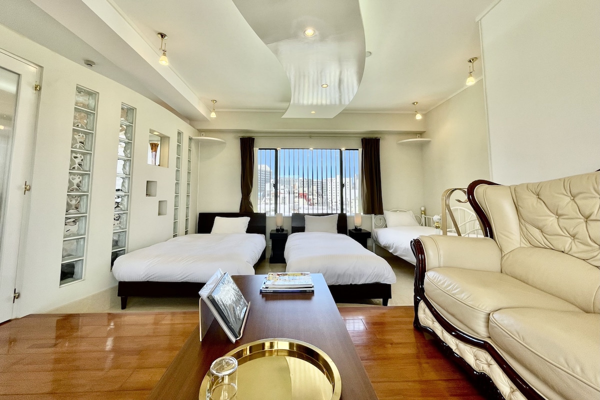 A hotel room with two beds, a sofa, a wooden coffee table, and a view of the city.