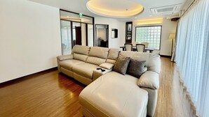 Uma sala de estar moderna com um sofá seccional bege, uma área de jantar com mesa e cadeiras, e uma grande janela que oferece luz natural.