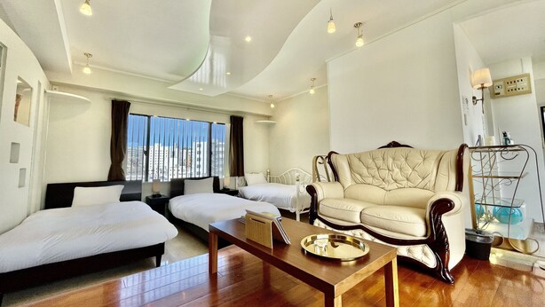 Quarto de hotel moderno com uma grande janela, um sofá, duas camas, uma mesa de centro de madeira e uma estante de metal.