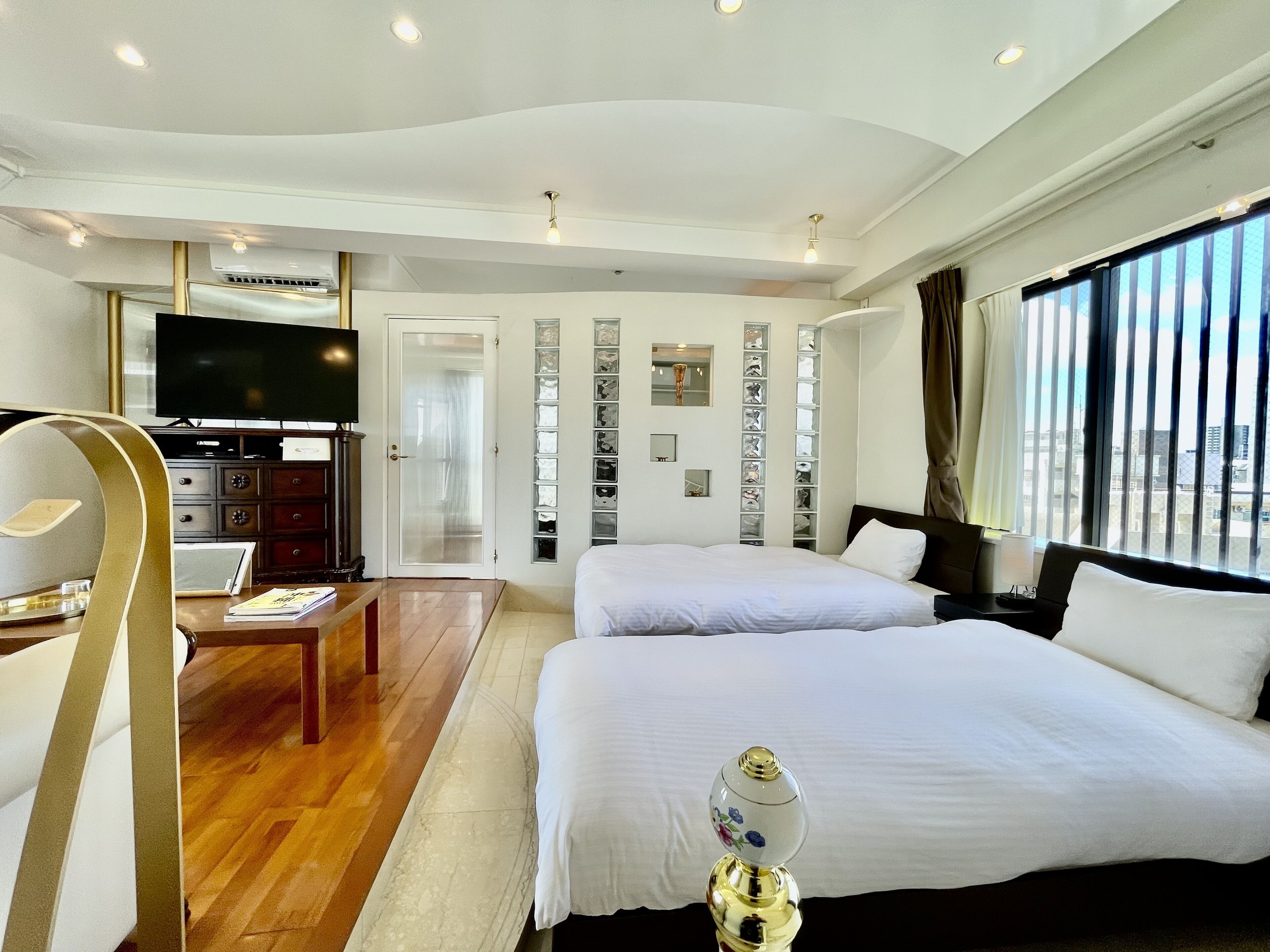 A hotel room with a large bed, a desk with a chair, a television, and a view of the city through the window.