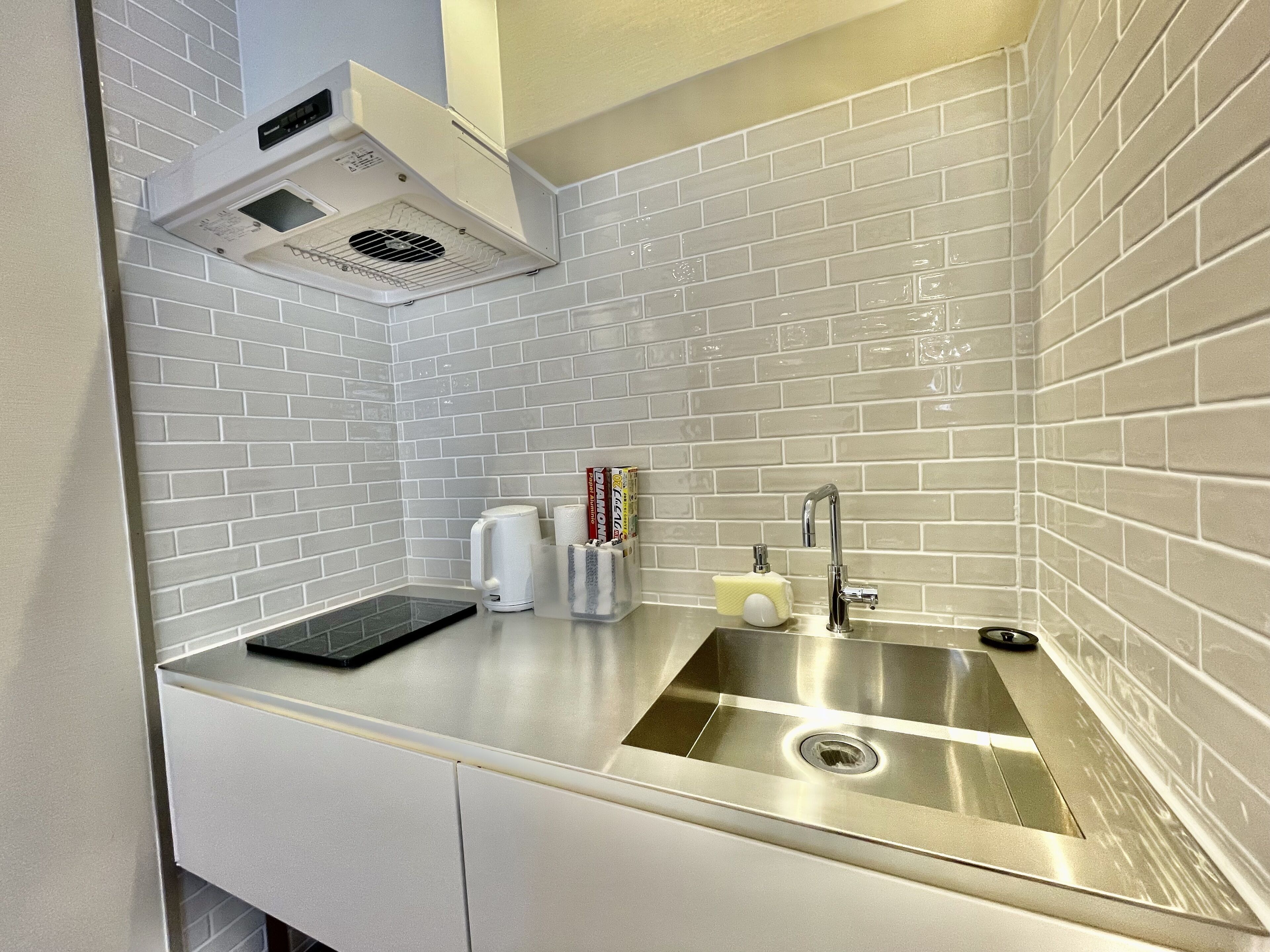 Una cucina con pareti rivestite di piastrelle bianche, un lavello in acciaio inossidabile e una cappa aspirante integrata.