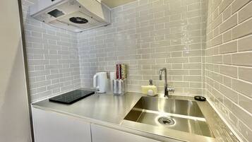Una cucina con pareti rivestite di piastrelle bianche, un lavello in acciaio inossidabile e una cappa aspirante integrata.