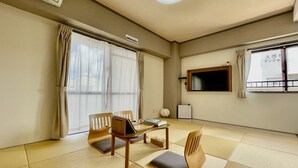 Quarto com piso de tatame, televisão fixada na parede e janela com cortinas.