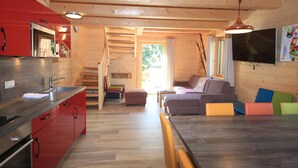 A modern kitchen with red cabinets, a stainless steel sink, and a wooden dining table. - Lodge with sauna in the centre of Kaprun (Kaprun)