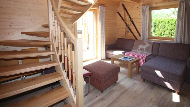 A wooden cabin interior with a staircase, a sofa, a small table, and a window with curtains. - Lodge with sauna in the centre of Kaprun (Kaprun)