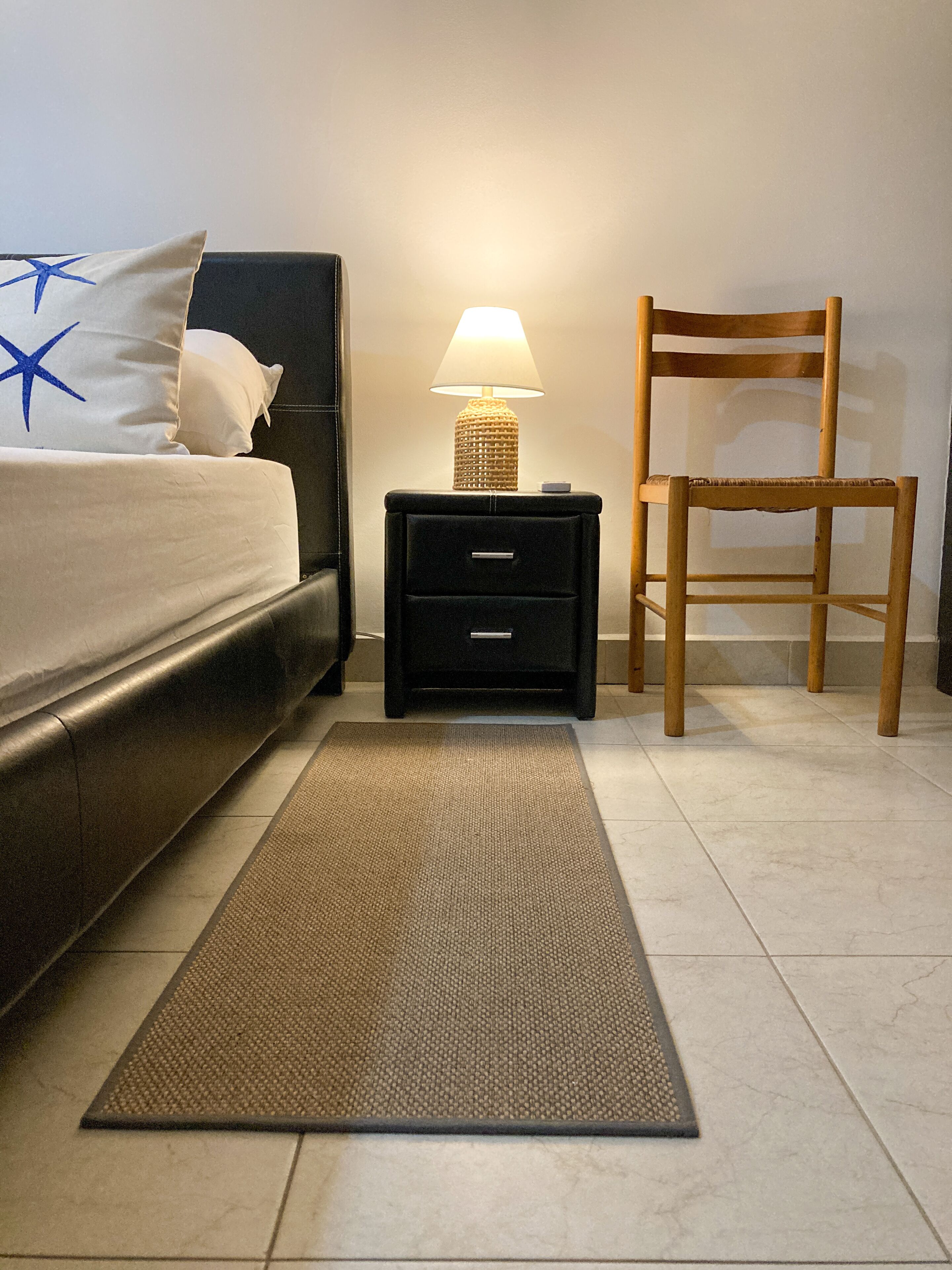 Un dormitorio con una cama, una mesita de noche con lámpara, una silla y una alfombra.