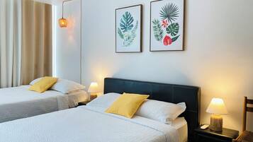 A hotel room with two beds, a nightstand with a lamp, and two framed botanical prints on the wall.