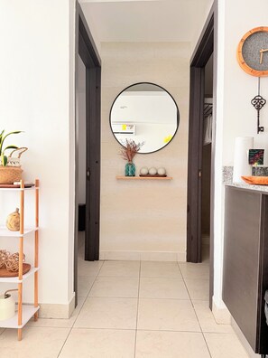 Un pasillo con un espejo redondo, un estante con adornos y una puerta que da a otra habitación.