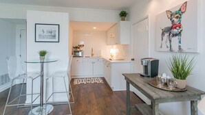 Een moderne keuken met witte kastjes, een koffieapparaat en een schilderij van een hond.