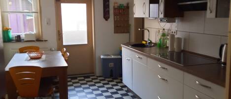 Una cocina con piso a cuadros, una mesa de comedor con sillas, armarios y un ventanal con persianas.