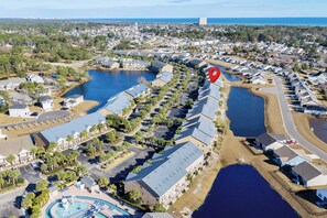 An aerial view of a residential area with multiple houses, a swimming pool, and a large body of water. - Surfside Stories 1st Floor Free Parking By Beach Star (Myrtle Beach)