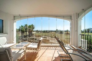 Un balcon avec une porte vitrée, des meubles blancs et une vue sur un terrain de golf.