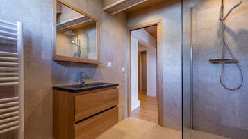 A modern bathroom with a wooden vanity, a glass shower enclosure, and a visible hallway.