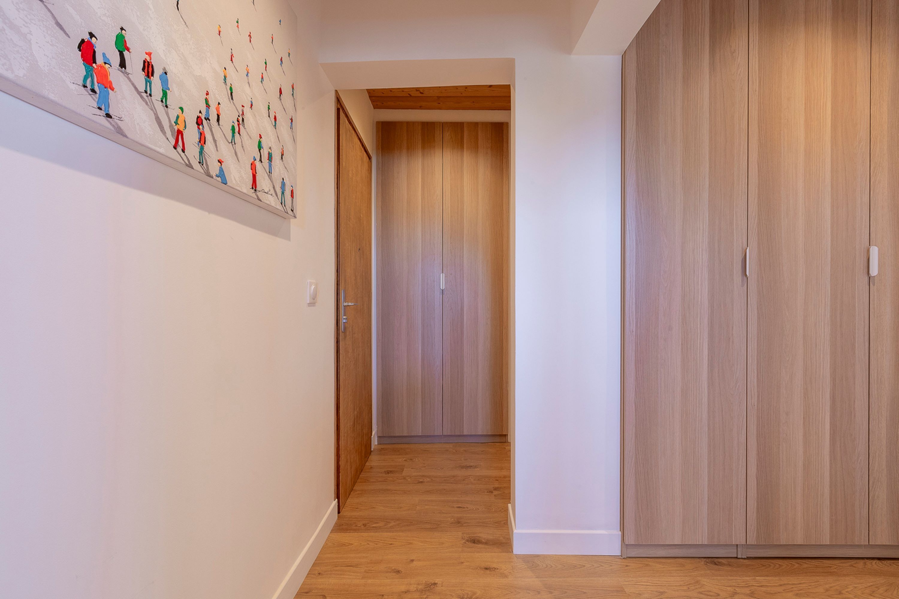 Un couloir doté d’un parquet en bois, d’une armoire en bois et d’un mur orné d’un tableau abstrait aux couleurs vives.