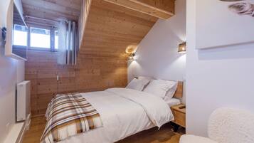 A bedroom with a wooden ceiling, a bed with white bedding, a nightstand, a wall-mounted light, and a window with curtains.