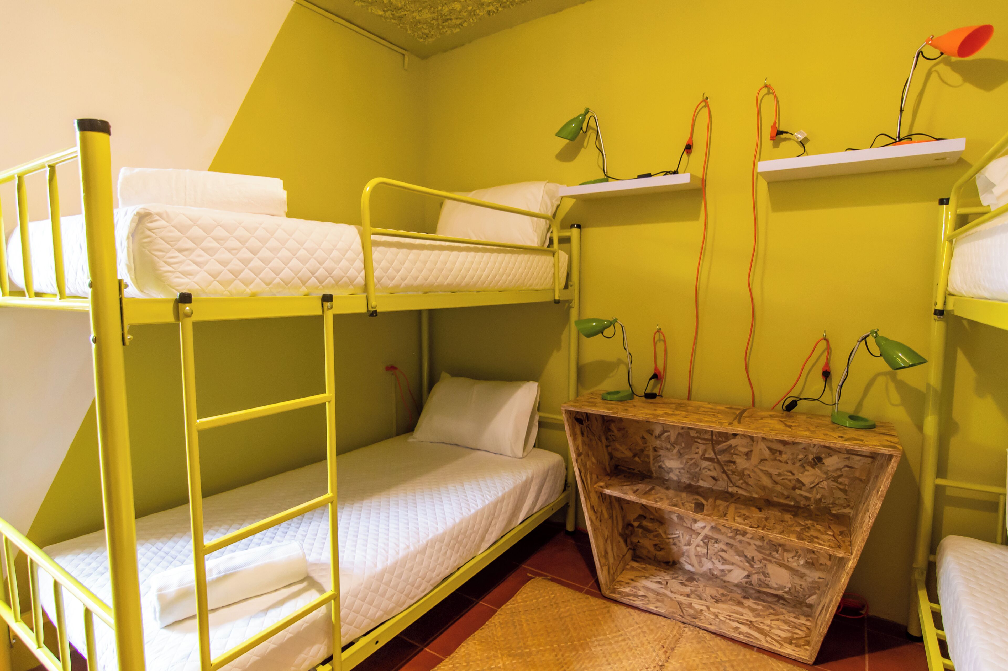 A dormitory room with bunk beds, a wooden desk, and two lamps.