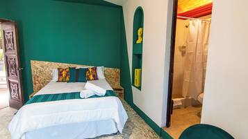 A bedroom with a bed, a wooden headboard, a green wall, and a bathroom visible through an open door.