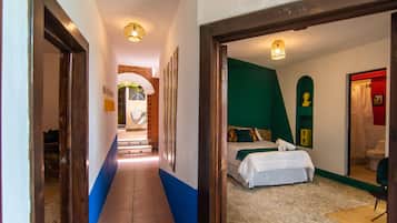 Un couloir d’hôtel mène à une chambre dotée d’un lit, d’un mur d’accent vert et d’une salle de bain visible à travers une porte ouverte.