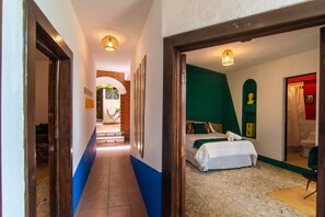 Pasillo de hotel que lleva a una habitación con una cama, una pared de acento verde y un ba ño visible a través de una puerta abierta.