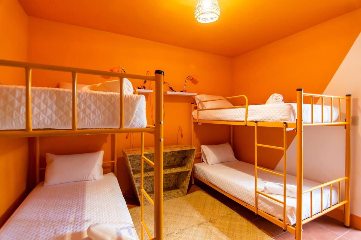 A dormitory room with bunk beds, a small wooden table, and a hanging light fixture.