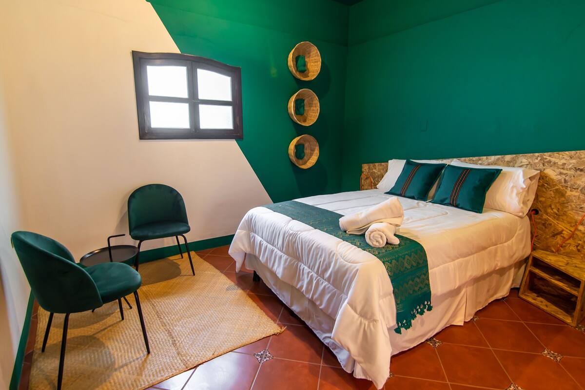A room with a bed, two chairs, a small table, a window, and three wall-mounted baskets.