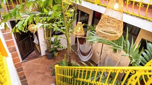 Una escalera con barandas amarillas, rodeada de plantas en macetas y lámparas de mimbre colgantes.