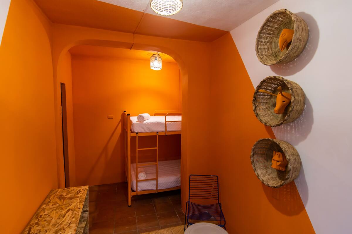 A bunk bed with a ladder, a chair, and three baskets on the wall.