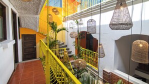 Un interior con varios niveles, barandilla amarilla, lámparas colgantes de mimbre y una escalera.