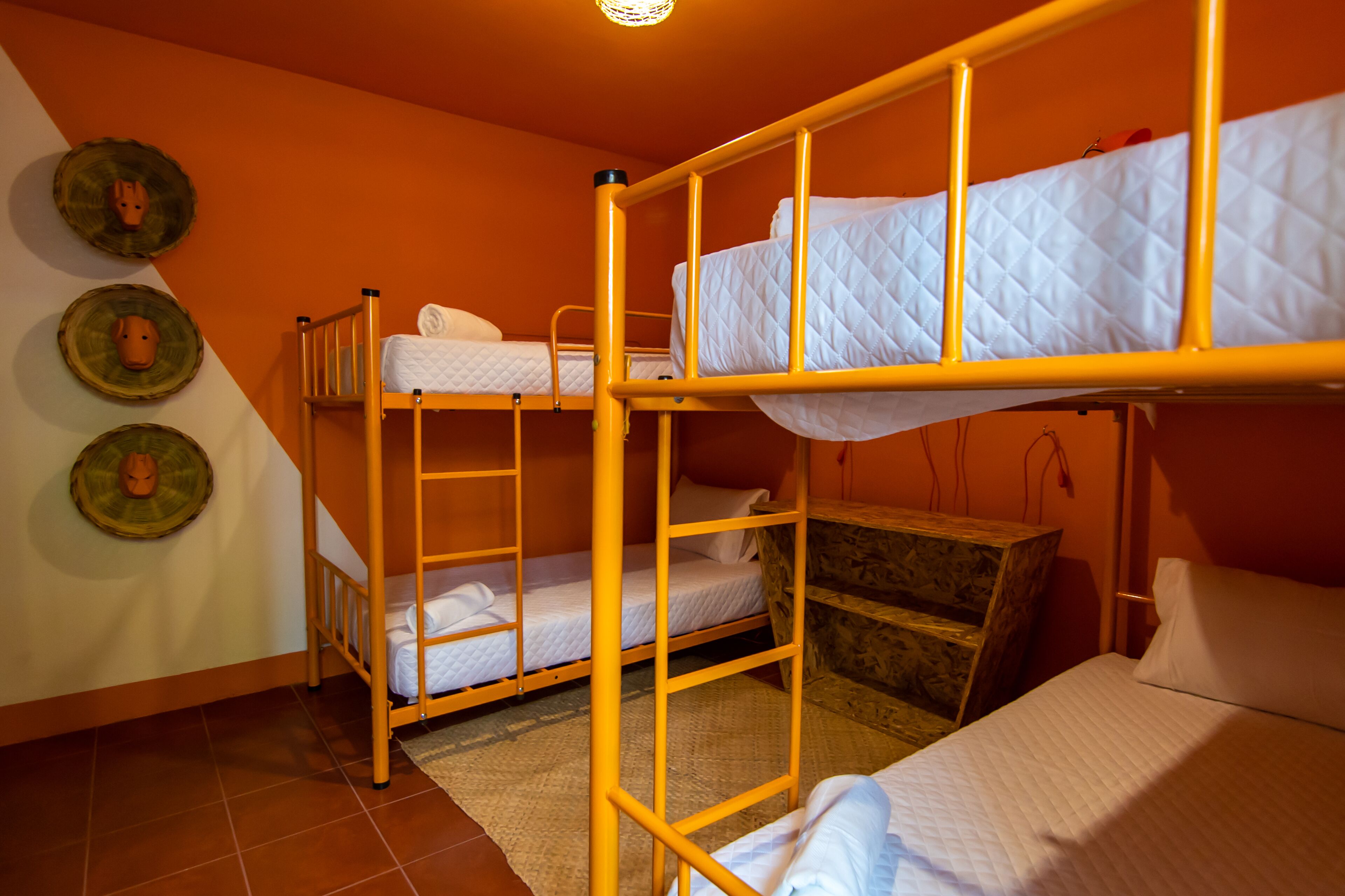Habitación con literas, una escalera de madera, un pequeño cofre de madera y tres placas decorativas colgadas en la pared.