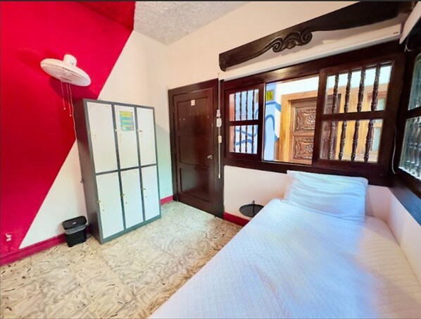 Una habitación con cama, armario, ventana con rejas y pared roja.