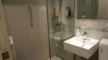 A modern bathroom with a glass-enclosed shower, a white sink with a mirror above it, and a glass shelf with toiletries.