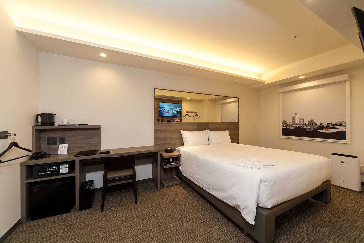 A hotel room with a bed, desk, and a television.