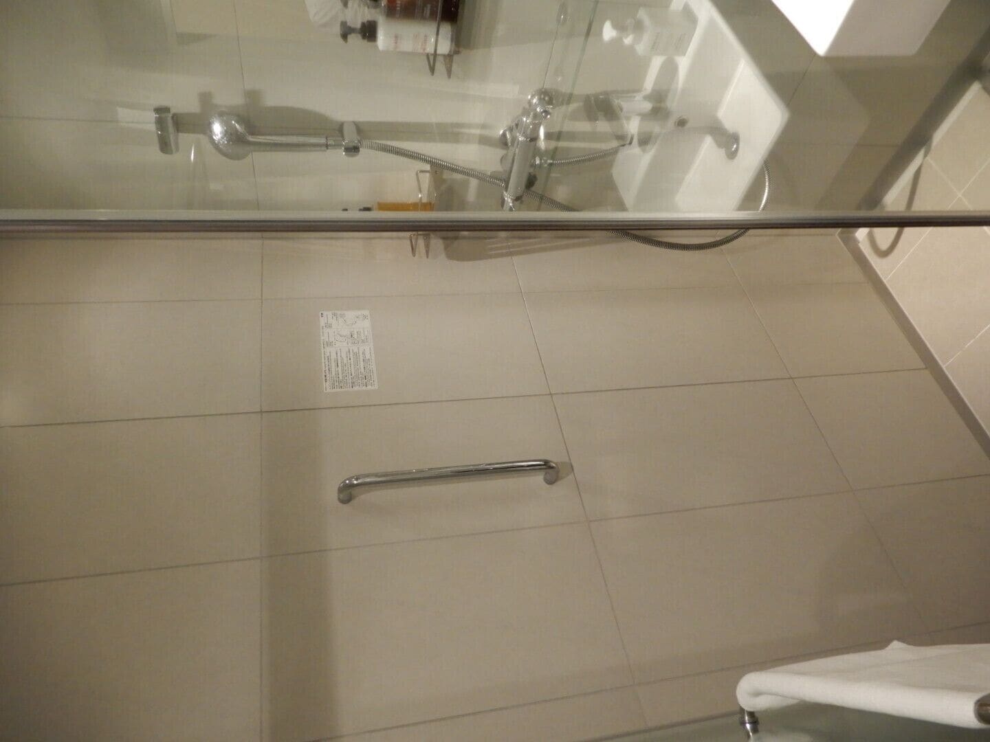 A bathroom with a glass shower enclosure, a handheld showerhead, a handheld shower control, and a white towel rack.
