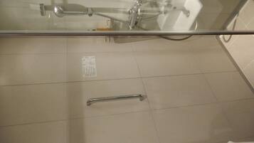 A bathroom with a glass shower enclosure, a handheld showerhead, a handheld shower control, and a white towel rack.