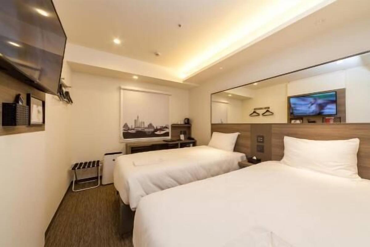 A hotel room with two beds, a desk, a TV, and a mirror.
